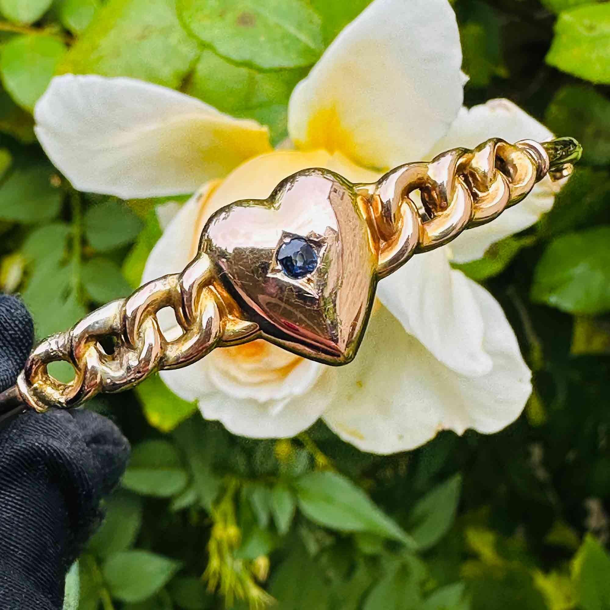Victorian 9ct gold bangle featuring a central sapphire heart, showcasing timeless antique charm displayed against garden.