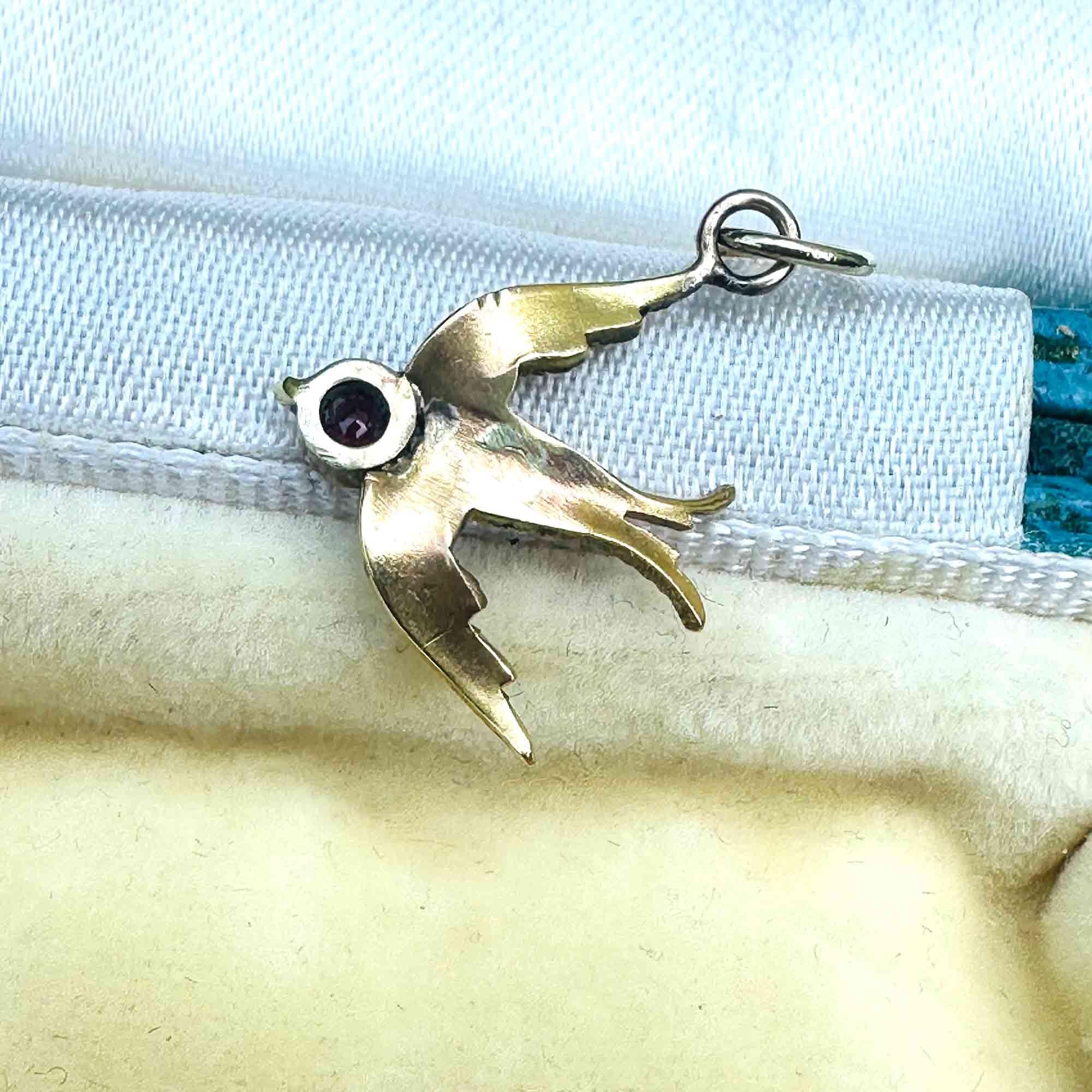 Close-up of antique 15k gold swallow charm showing fine detail and ruby-set head, back view