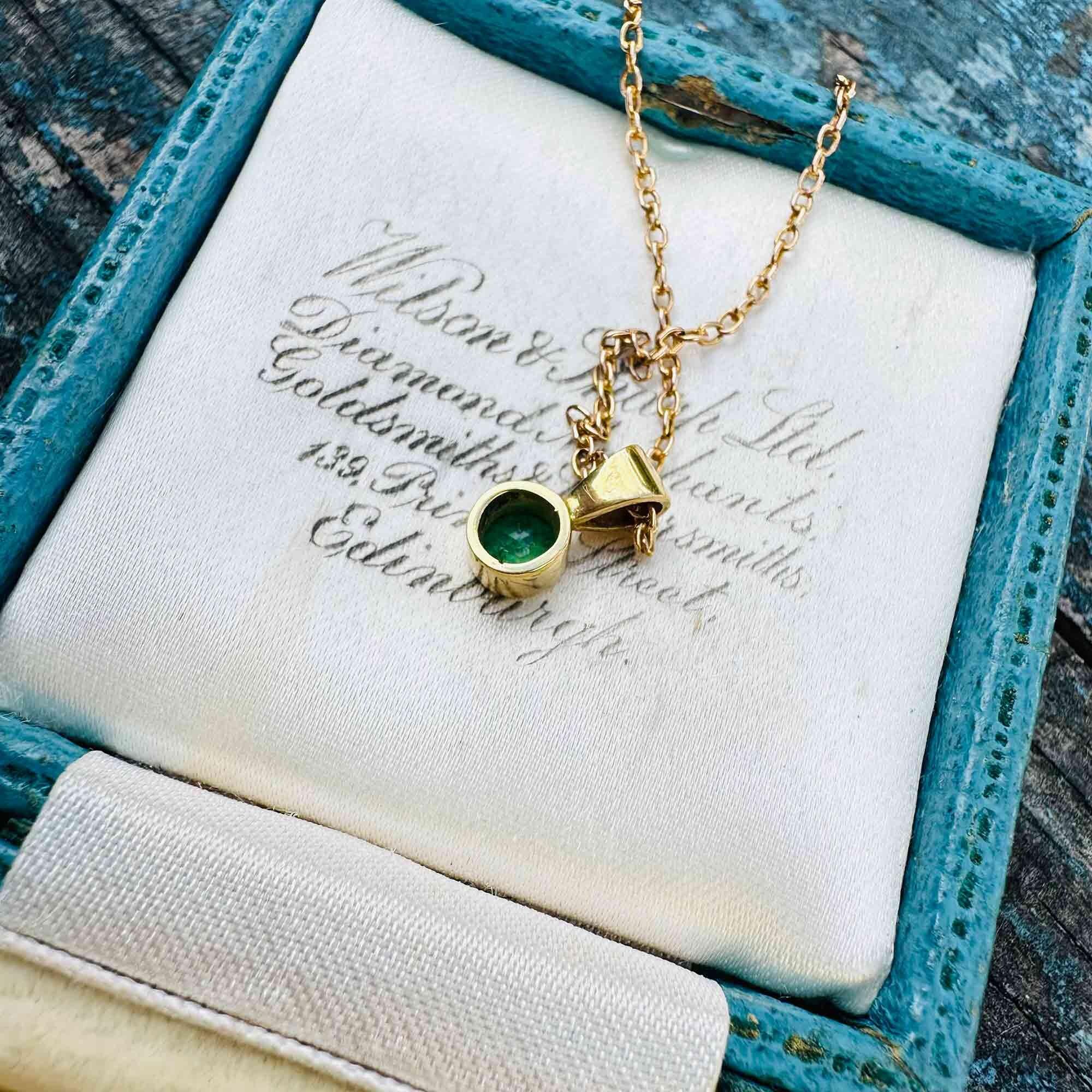 back view  of 18ct gold emerald solitaire pendant with a round bezel-set emerald, displayed on a antique box.
