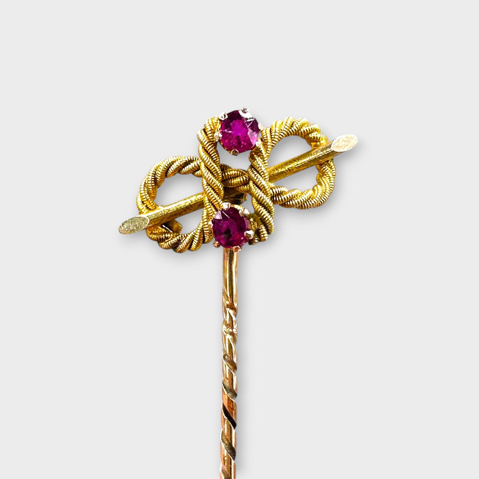 Edwardian 9ct yellow Gold Faceted Ruby Knot Stick Pin on grey background.