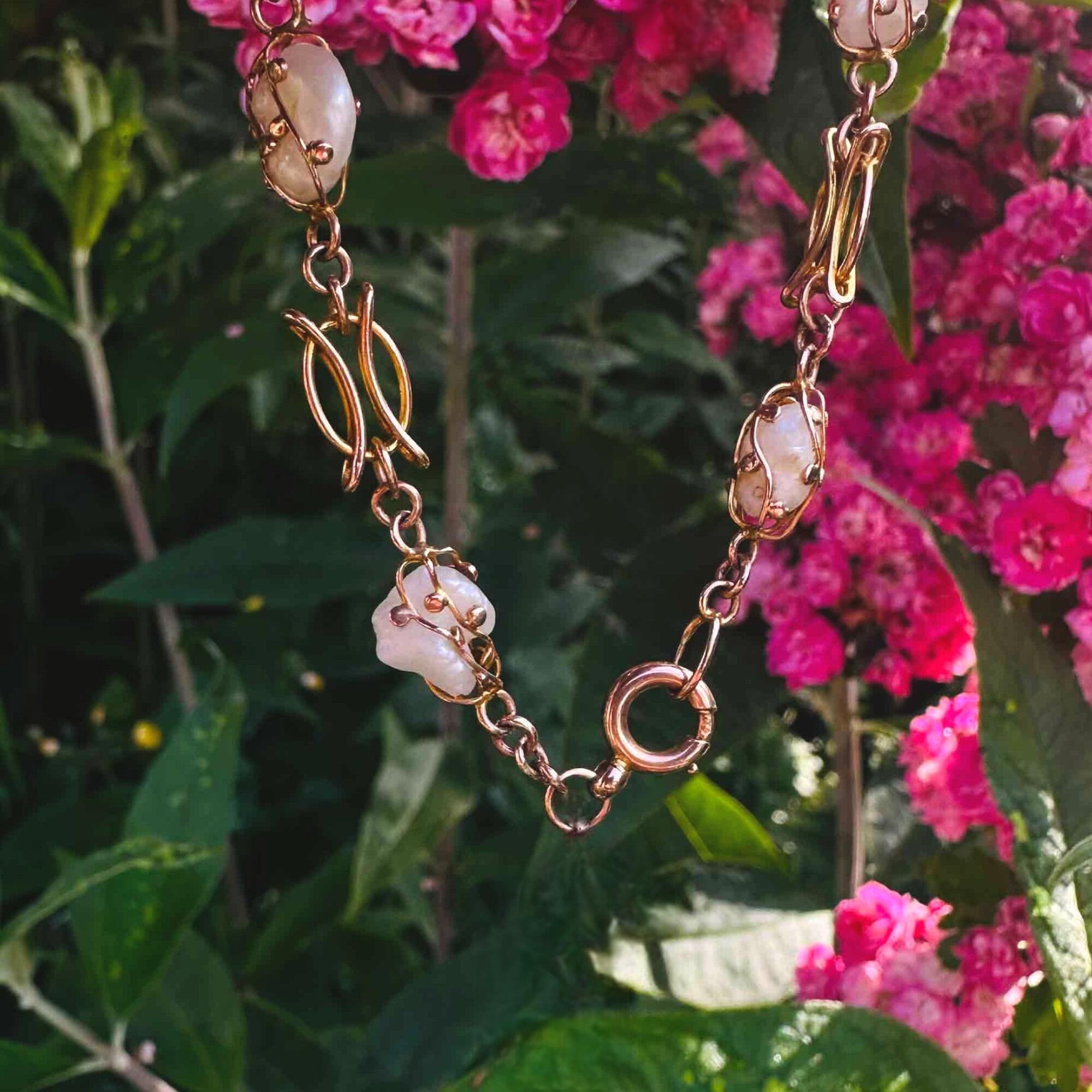 Art nouveau 9k rose gold cage pearl bracelet held in hand in garden