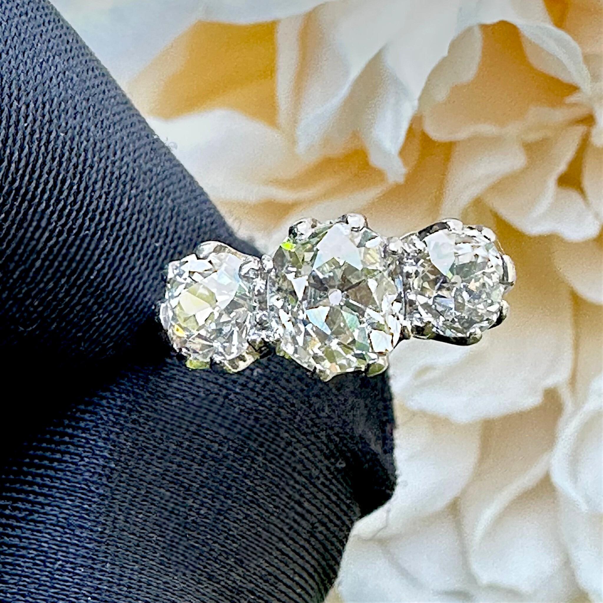 Antique Platinum Old Cushion Cut Diamond Trilogy Ring held in gloved hand  with flower background