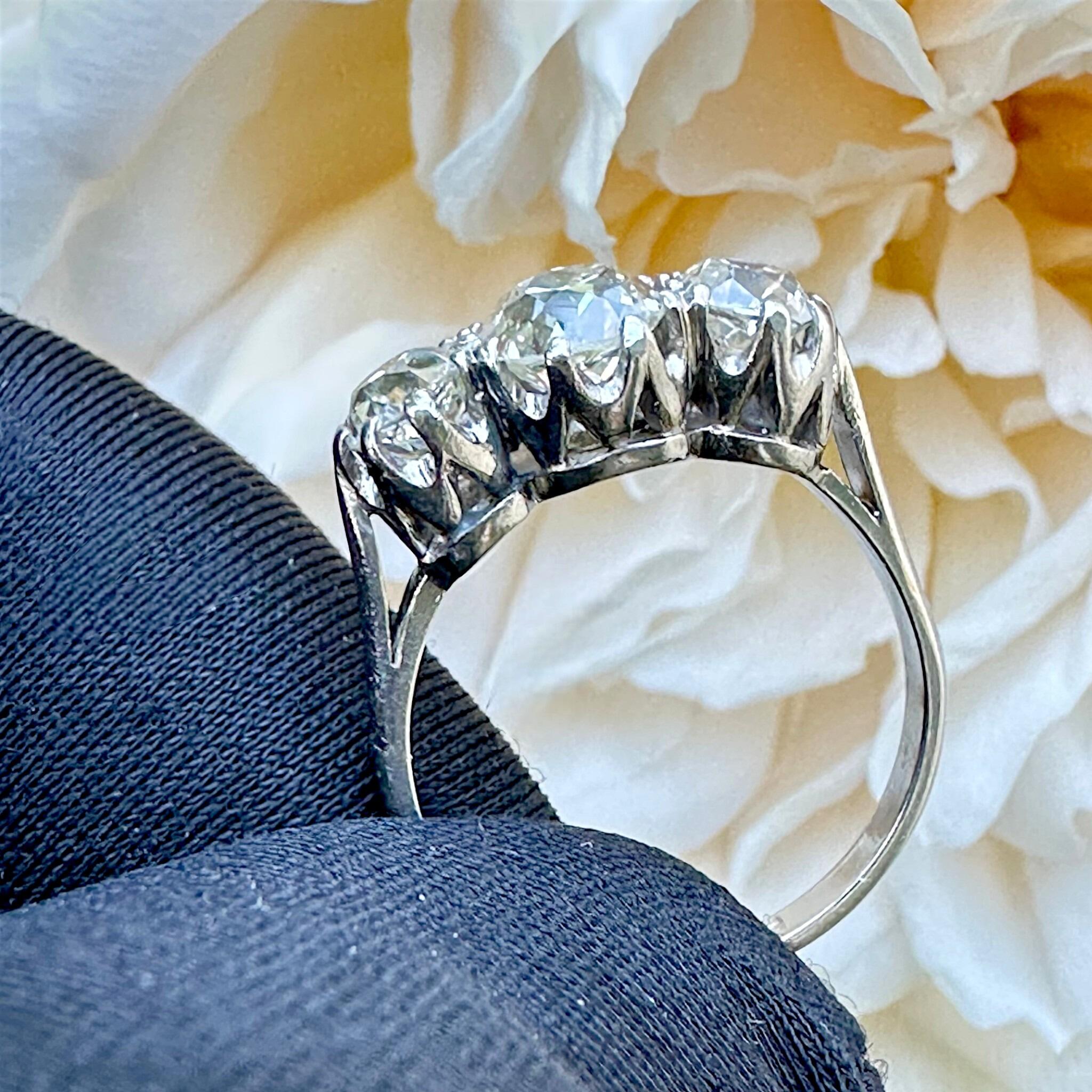 side view of Antique Platinum Old Cushion Cut Diamond Trilogy Ring, with flower in the background