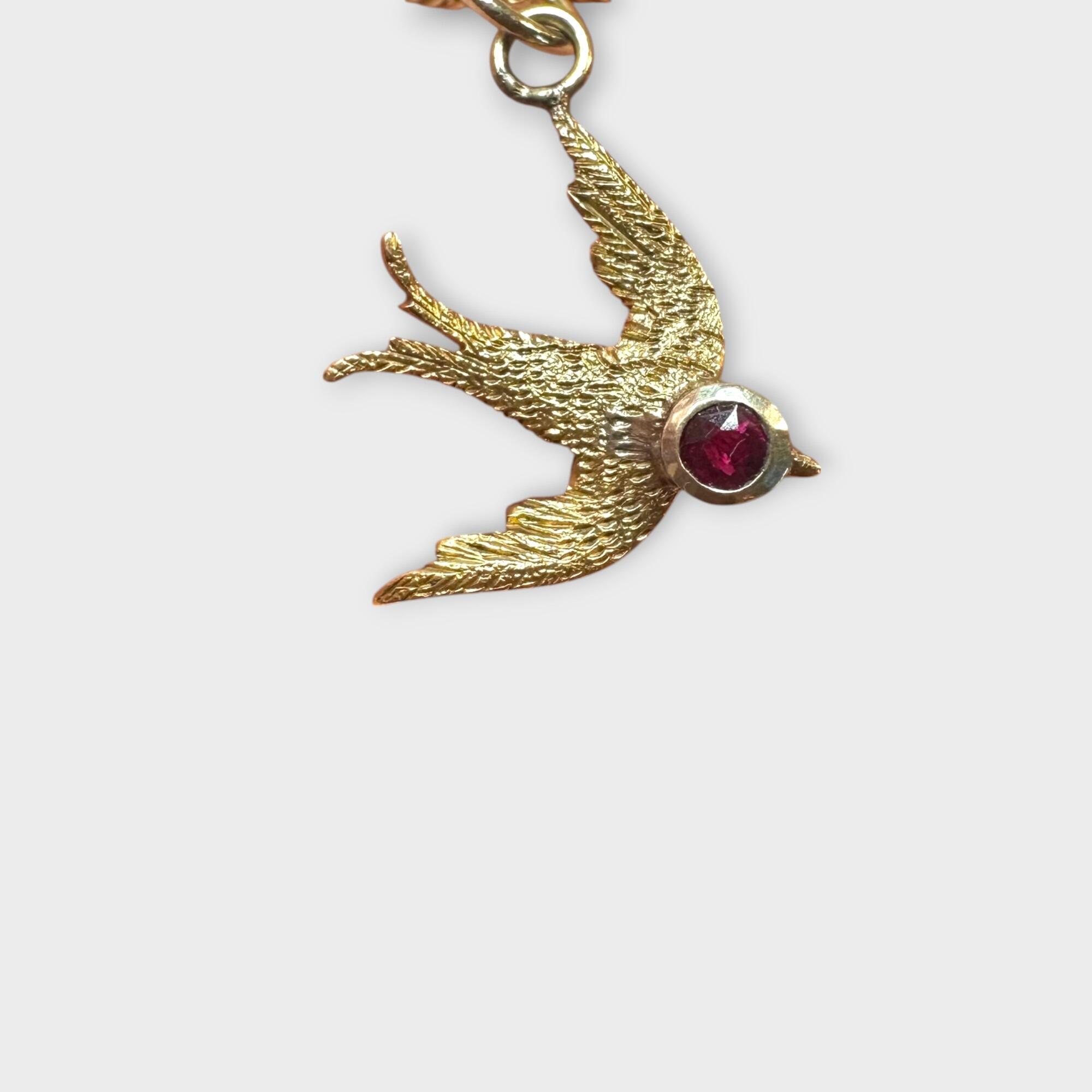 Antique 15k gold swallow charm showing fine detail and ruby-set head, grey background