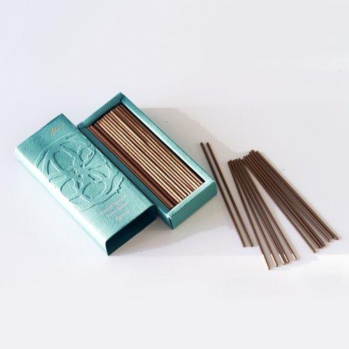 A pale green box open with the lid off showing brown incense sticks inside. Some incense sticks are scattered in a pile next to the box.