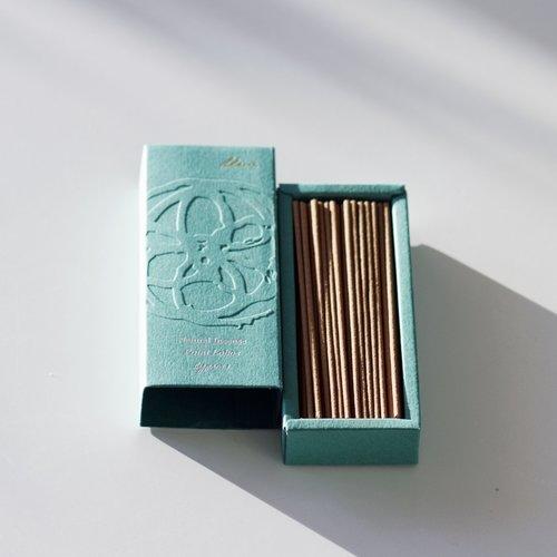 A pale green box open with the lid off showing brown incense sticks inside.