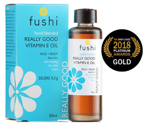 a brown glass bottle with black cap. stood next to light blue box packaging. Label shows fushi really good vitamin e oil.
