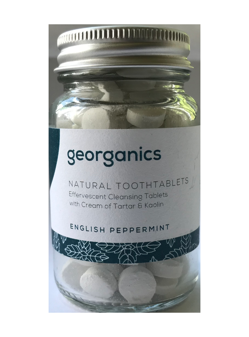 A clear glass jar containing small round tablets. Jar has screw top silver aluminium lid. Label shows georganics natural toothtablets english peppermint.