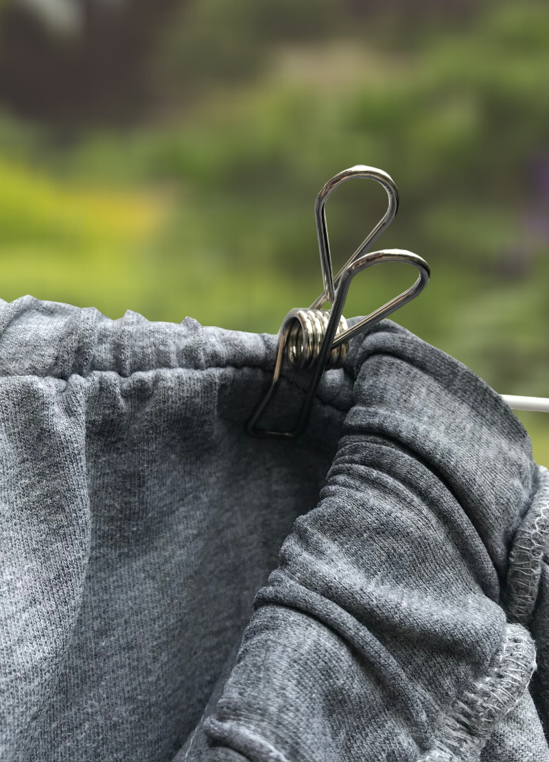 Silver stainless steel peg clipped onto grey garment on white garden washing line.