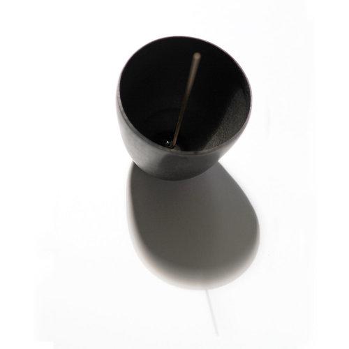 Black porcelain curved pot shown with brass incense holder inside with incense stick inserted.