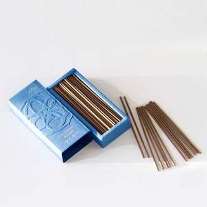 A pale blue rectangular box with lid off next to it. The open box is filled with long brown incense sticks. A few incense sticks are displayed in a pile next to the box.