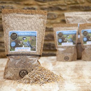 Brown Natural Bags with clear windows showing bird seed label shows no mess wild bird food cotswold granaries. Displayed on a table with a pile of loose bird seed.