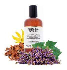 surrounded by herbs a brown plastic bottle with black cap and white label showing amphora sensuous bath oil