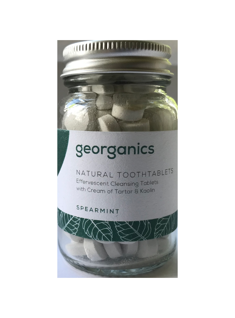 A clear glass jar containing round tablets. Jar has screw top silver aluminium lid. Label shows georganics natural toothtablets spearmint.