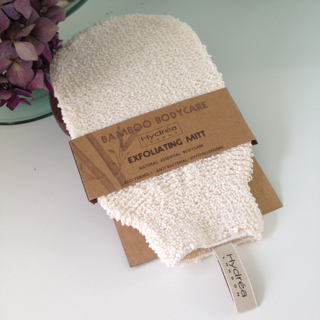 A cream textured fabric cleansing mitten, with natural brown card wrap around showing hydrea bamboo exfoliating mitt.