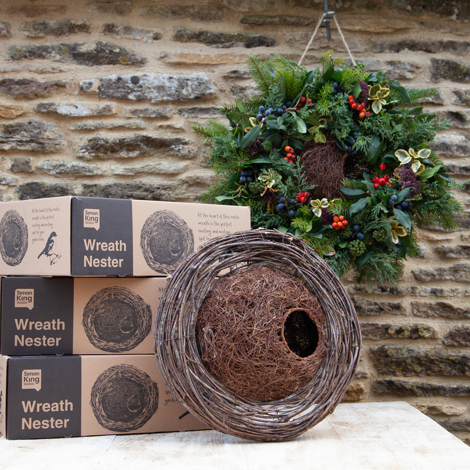 round brush wood wreath base wrapped around a ball shaped concealed bird nester. Displayed on an outside garden table with stacked cardboard boxes showing bird nester wreath
