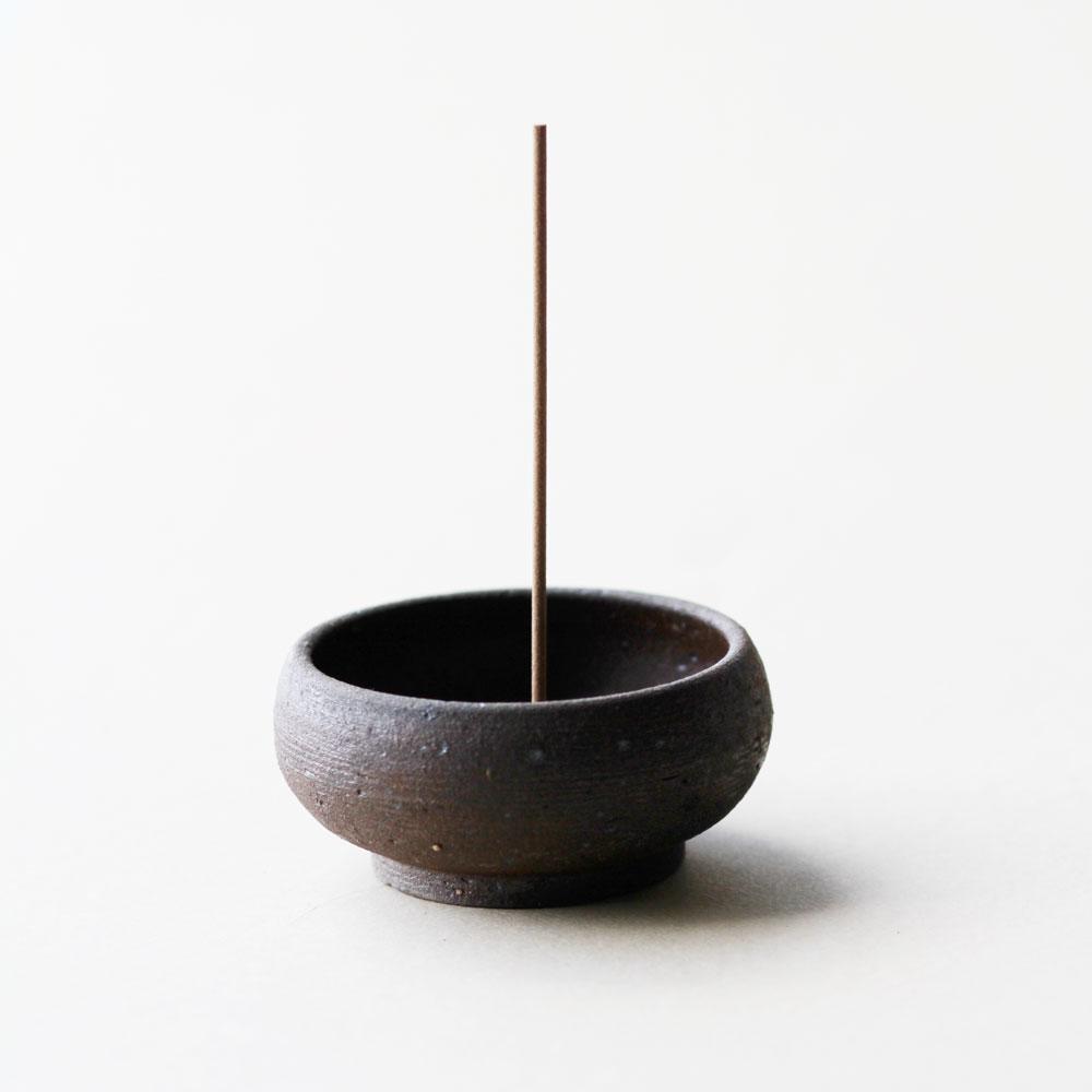 Side view of a small black clay bowl with incense stick inserted