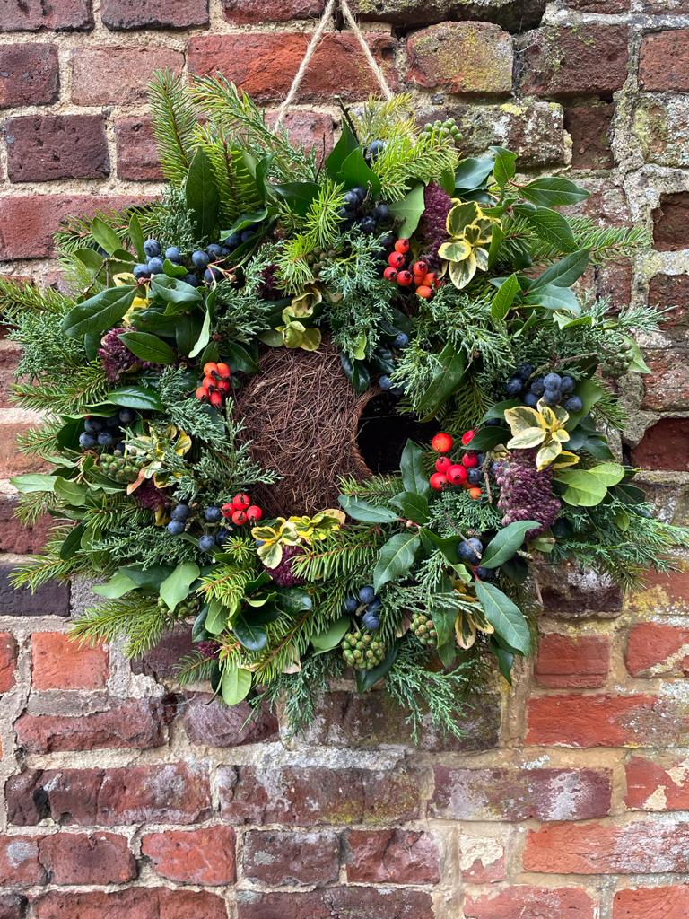A christmas wreath decorated with dark green holly foliage and hung against a brick wall