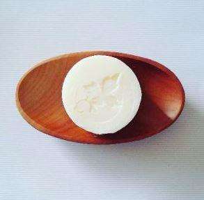Brown oval wooden soap dish showing round white bar of castile soap with imprinted pure nuff stuff leaf logo