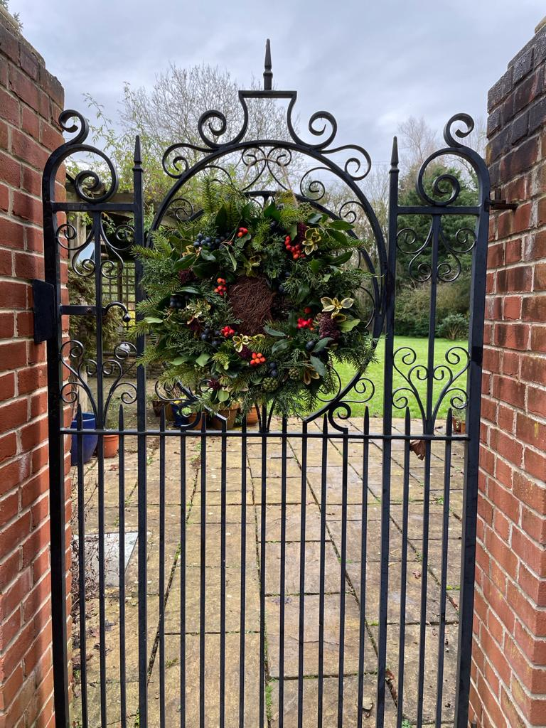 A christmas wreath decorated with dark green holly foliage and hung on a tall black wrought iron garden gate