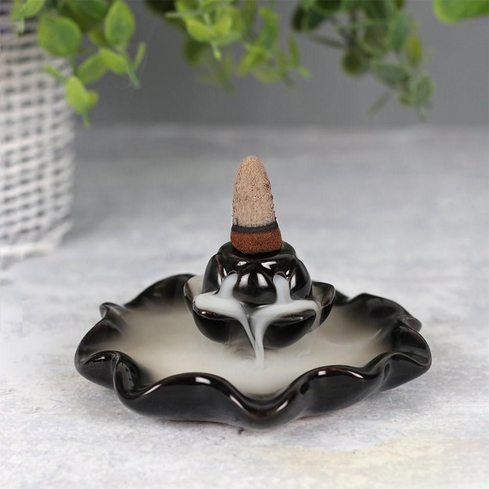 Backflow incense burner in a black ceramic lotus pool design, smoke cascades down in a waterfall effect, garden background.