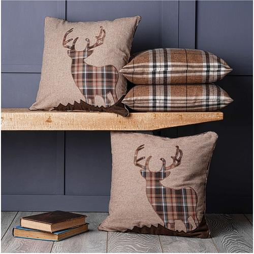 Four stag and tartan cushions, three on a wooden shelf and one below the shelf to the left of some books.