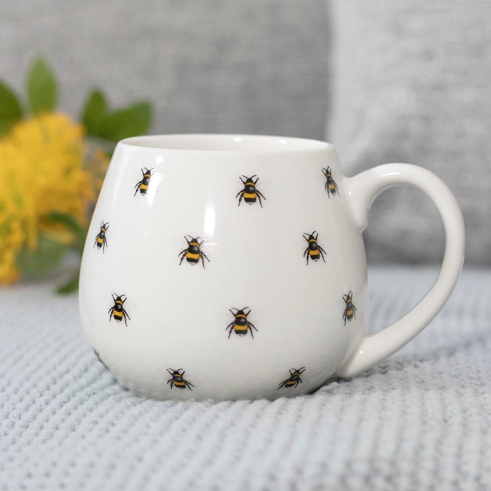 A white rounded mug with all over bee print, shown with a grey background.