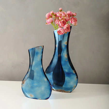 Two metallic blue metal vases, one large holding pink roses and one small.