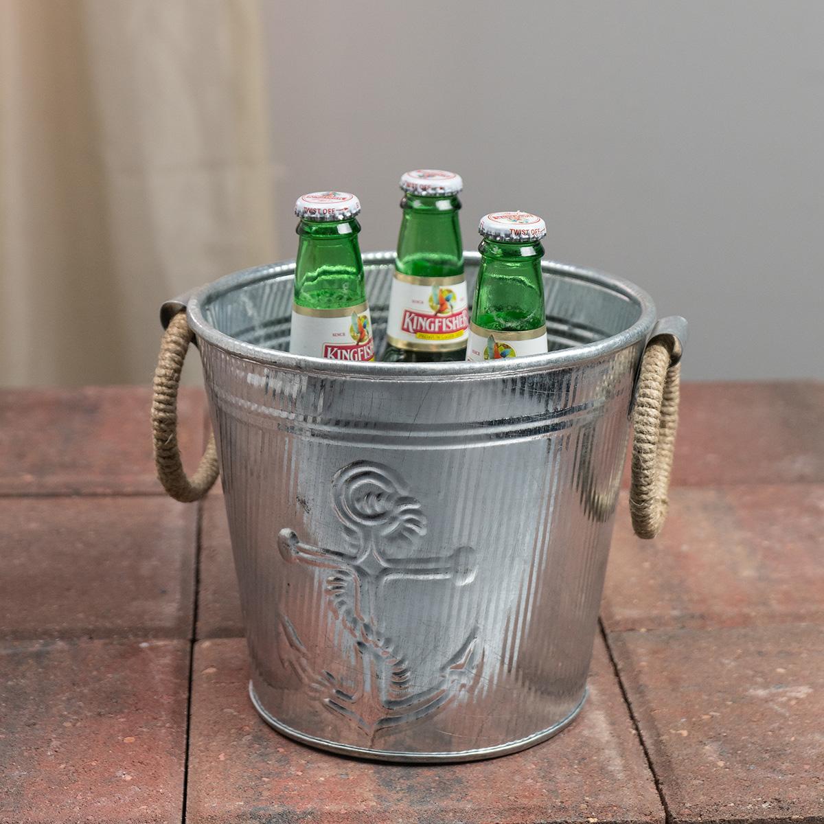 Galvanised metal ice bucket with rope handles and an anchor design, shown with kingfisher beer on a stone surface