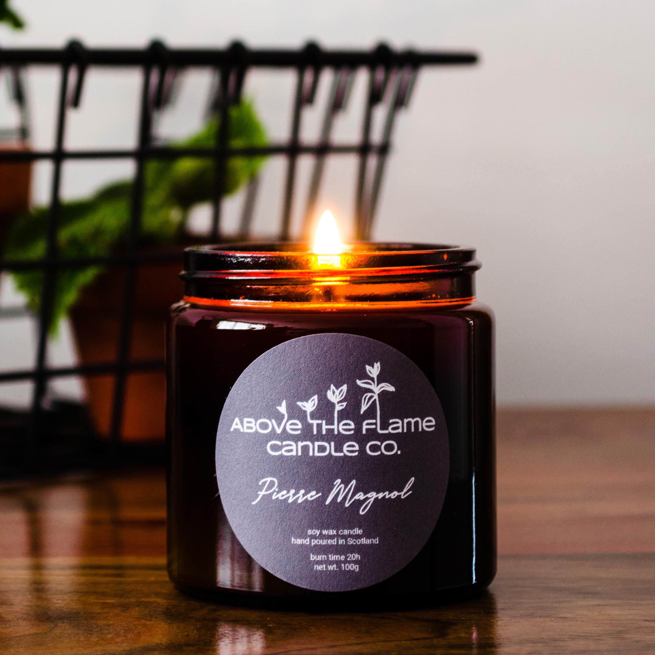 A lit pierre magnol amber soy wax candle jar handmade by above the flame candle Co on a wooden table