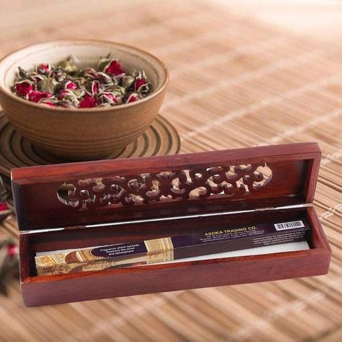 An open mango wood incense box with a box of incense sticks inside, sat on a bamboo runner in front of a bowl of pot pourri.