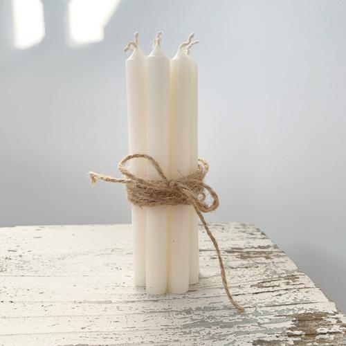 Six white dinner candles tied together with brown twine and stood on a rustic antique white table.