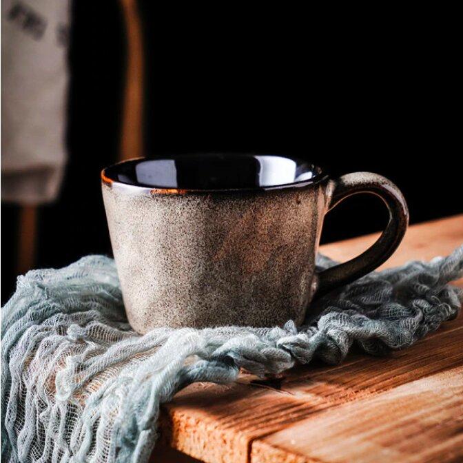 Light grey handmade retro ceramic mug, on a blue woven material on a wooden surface.