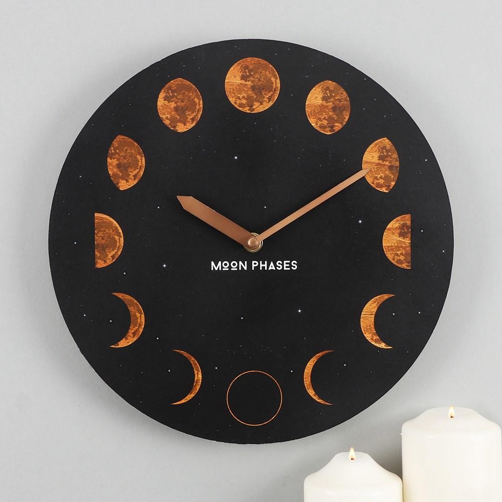 Round MDF black wall clock with moon phases design and 'moon phases' text, shown on a grey wall with candles below.
