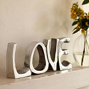 Recycled stainless steel 'Love' sign on a mantelpiece with a glass vase of yellow flowers.