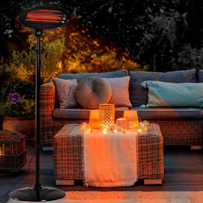 Cosy outdoor setting, including wicker furniture with grey pillows, candles, bulb lights and a standing patio heater.