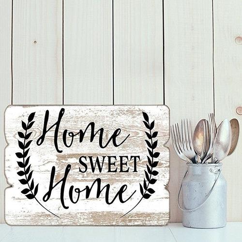 A rustic antique 'Home Sweet Home' plaque lent on a white wood panel wall and next to a small milk churn holding cutlery.