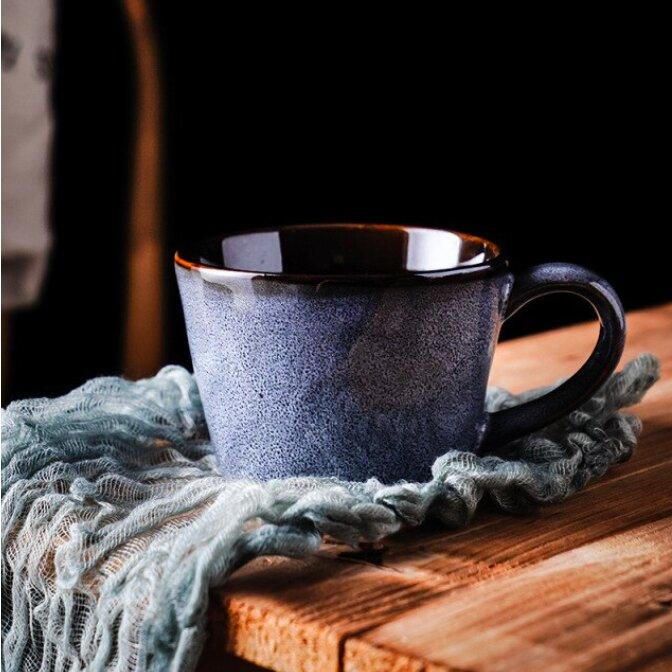 Blue handmade retro ceramic mug, on a blue woven material on a wooden surface.