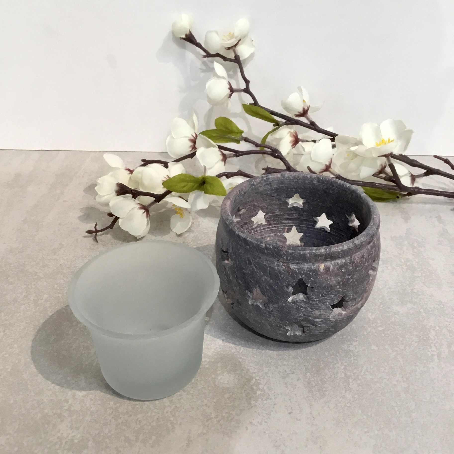 Stone votive tealight candle holder with star cutout design, on a grey surface in front of white flowers.