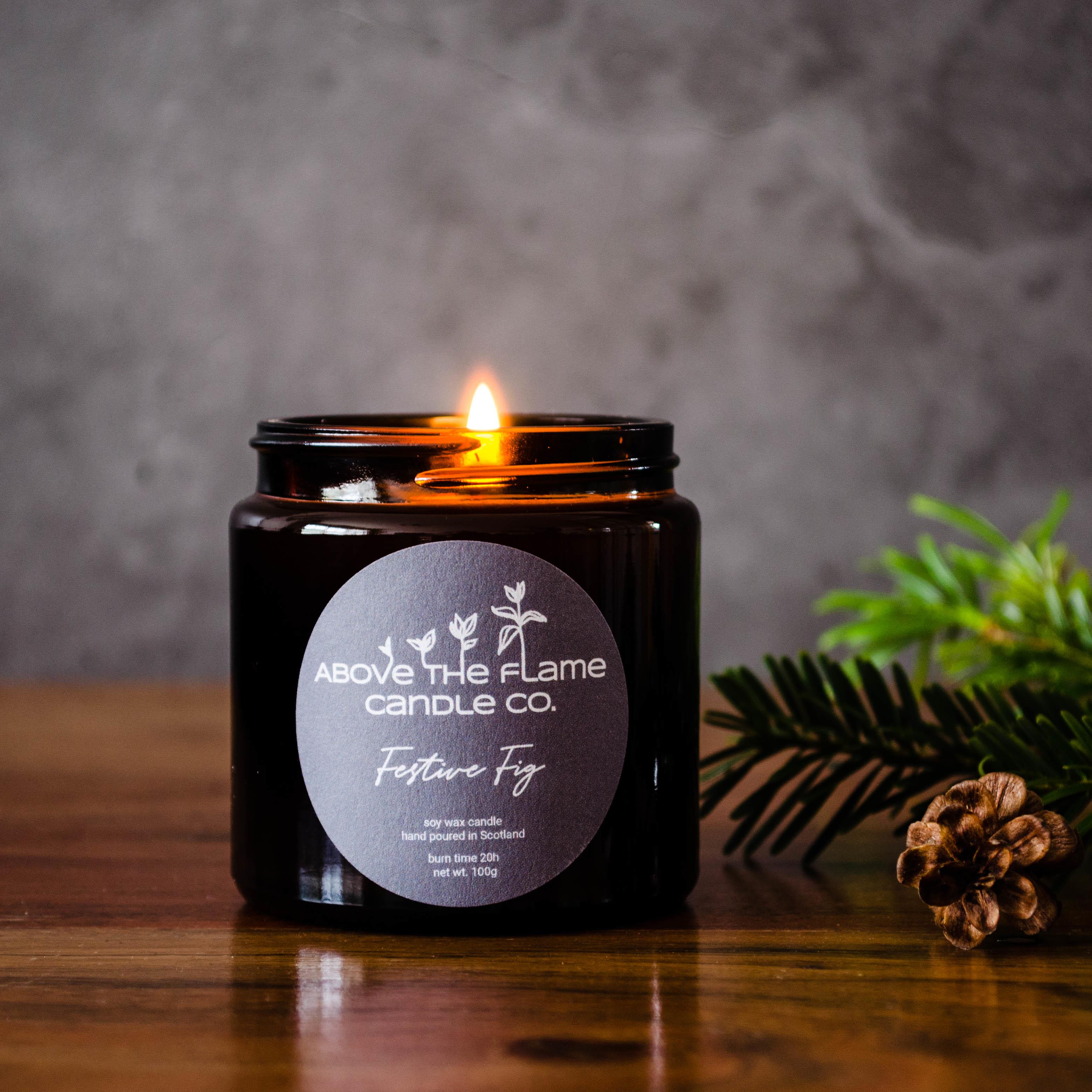 A lit festive fig amber soy wax candle jar handmade by above the flame candle Co on a wooden table