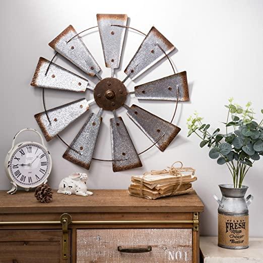 A rusty galvanised windmill wall piece above a wood sideboard that holds an antique white clock, rustic rabbit & other decor.