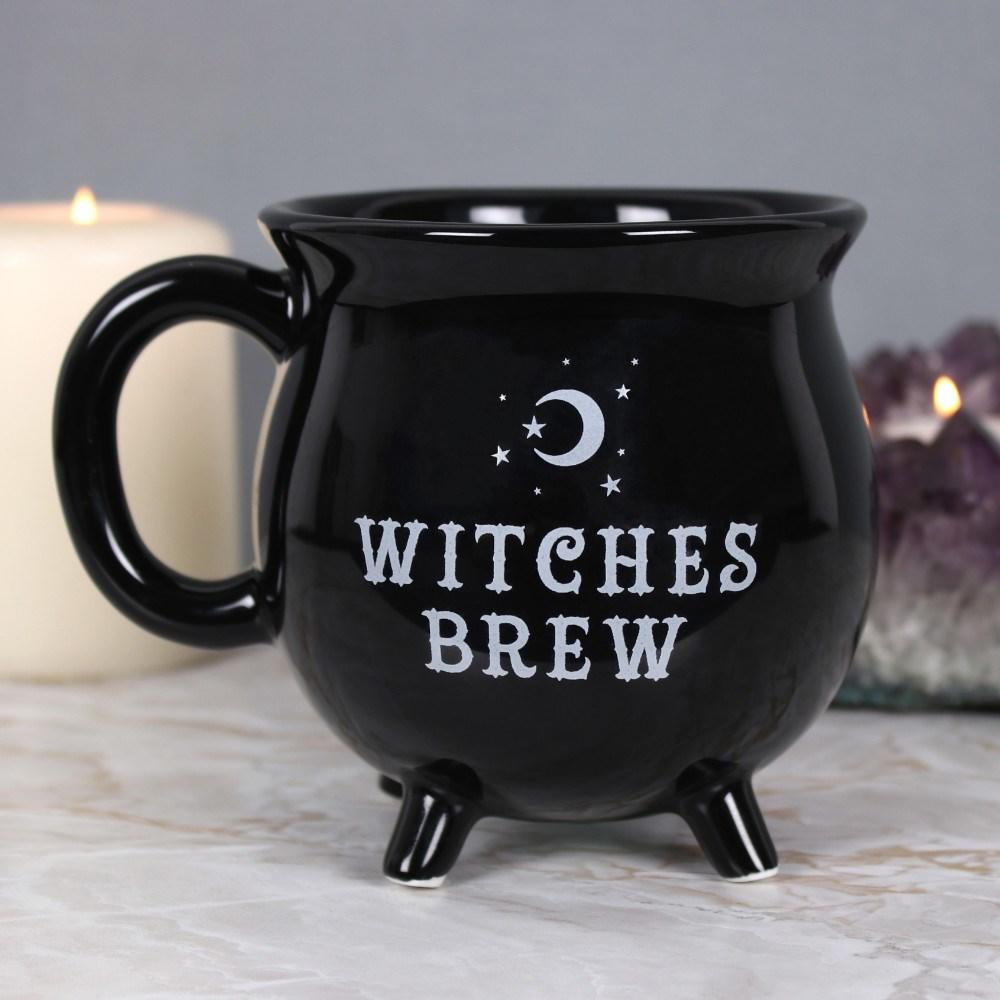 Black cauldron shaped mug with 'witches brew' text and a stars & moon design, on a grey surface with candles behind.