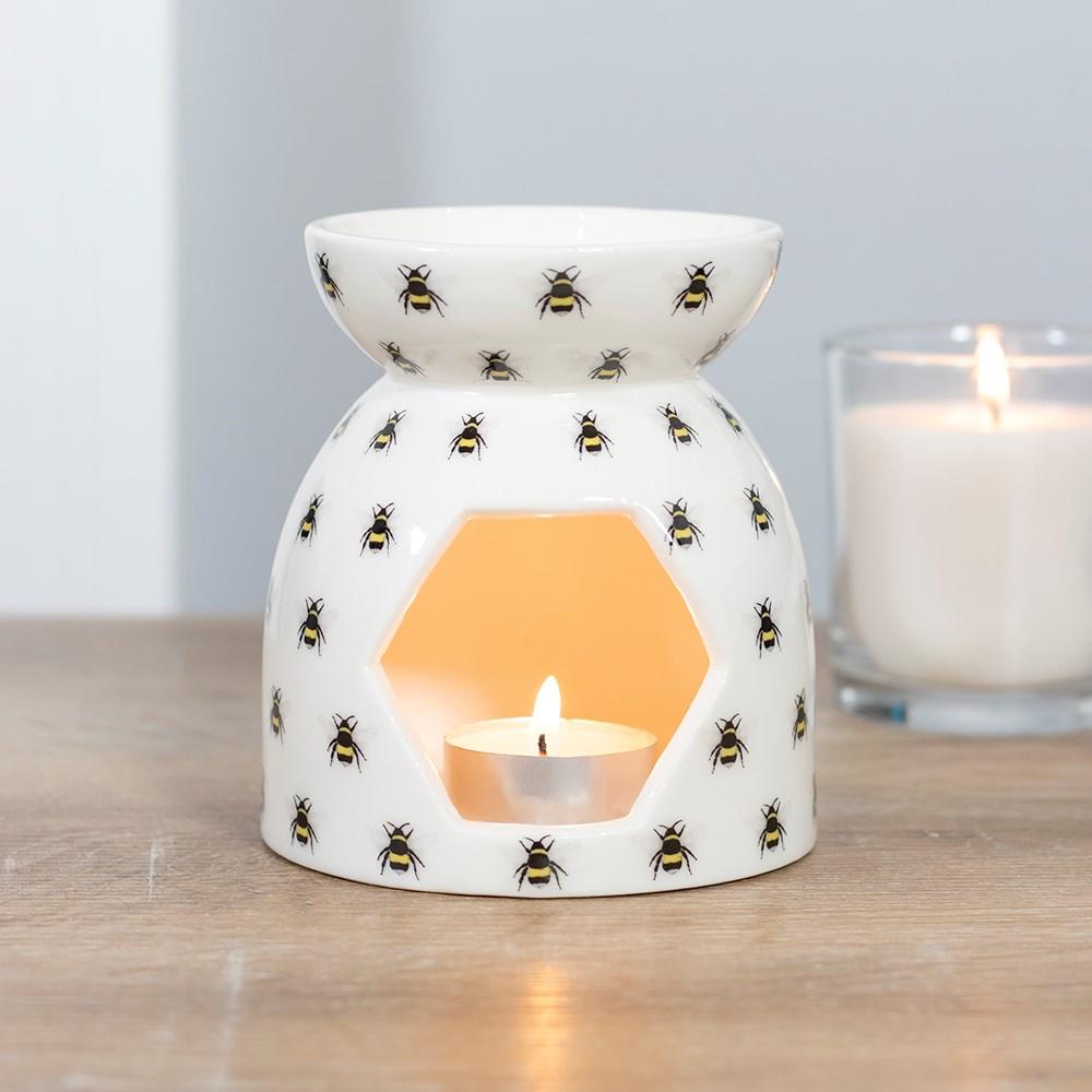 Shown on a wooden surface, All over Bee Print Ceramic Oil burner holding a lit tealight candle.