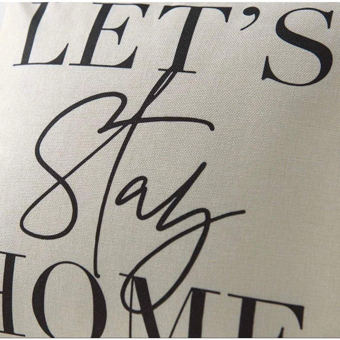 Cream throw cushion with black 'Lets Stay Home' text, close up.