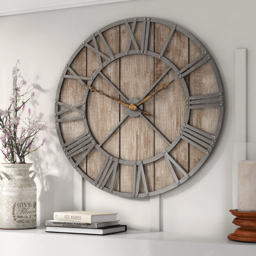 An oversized rustic wooden clock with grey roman numerals and rusty hands, on a white wall above a decorated white sideboard.