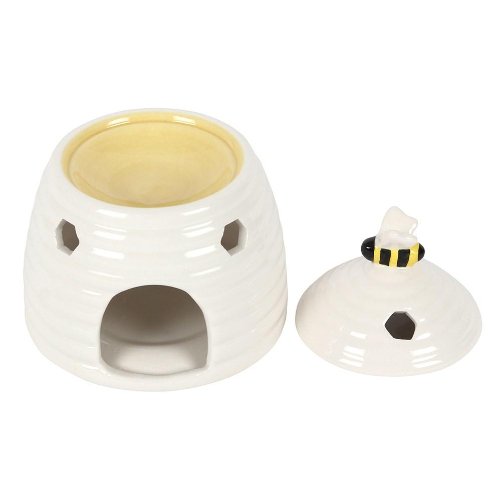 White ceramic oil burner & wax warmer in the shape of a beehive with a bee on the lid & honeycomb cutouts, lid removed.