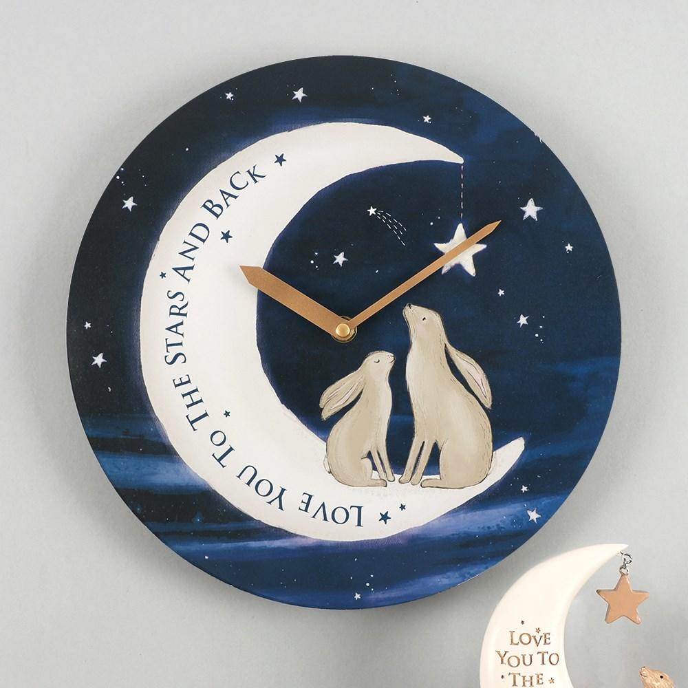 Round wall clock with a night sky design & two rabbits sat on a moon that reads 'Love you to the stars and back', on a wall.