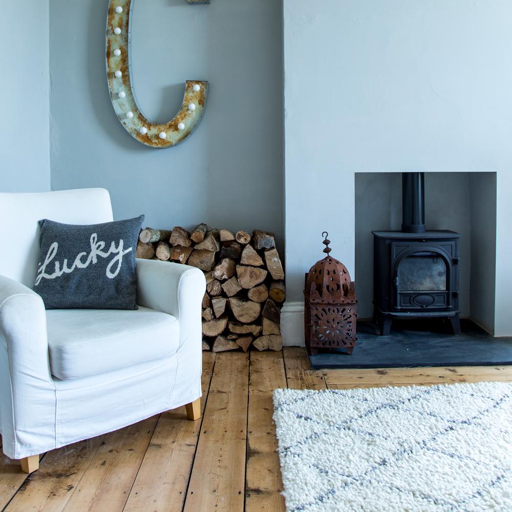 Living room setting with a fireplace, logs, letter c sign, a berber rug & a white sofa with a grey pillow that reads 'lucky'