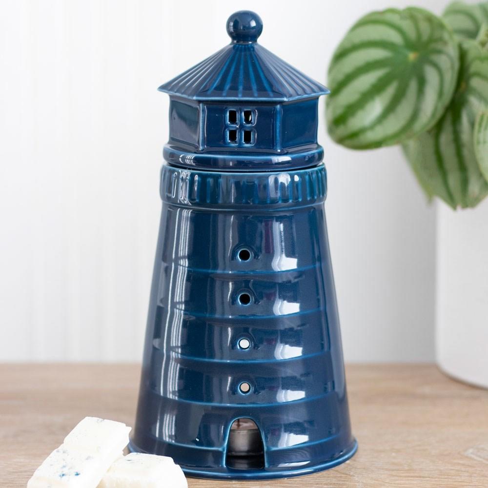 Blue light house lidded wax warmer and oil burner, on a wooden surface next to wax melts and in front of a plant.