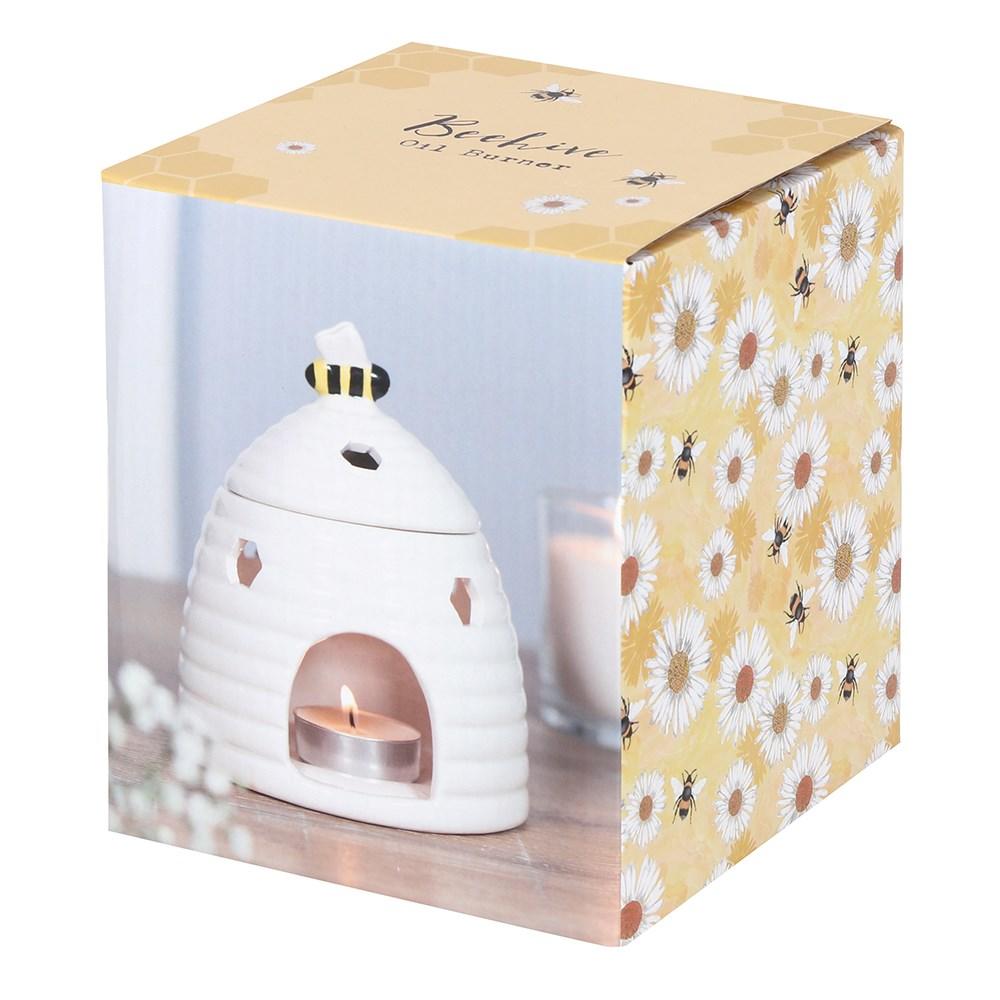 White ceramic oil burner & wax warmer in the shape of a beehive with a bee on the lid & honeycomb cutouts, shown in box.